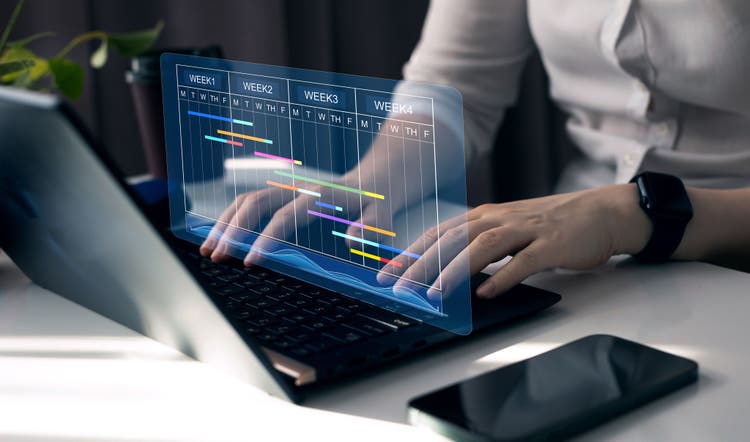 Project manager working on laptop and updating tasks and milestones progress planning with Gantt chart scheduling interface for company on virtual screen. Business Project Management System