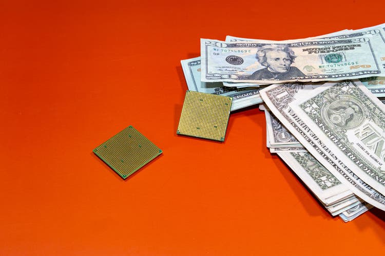 Two Microchips Next to Many Dollars on an Orange Surface